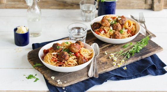 Zwei Teller mit Spaghetti und Hackbällchen in Tomatensoße auf einem Holzbrett angerichtet