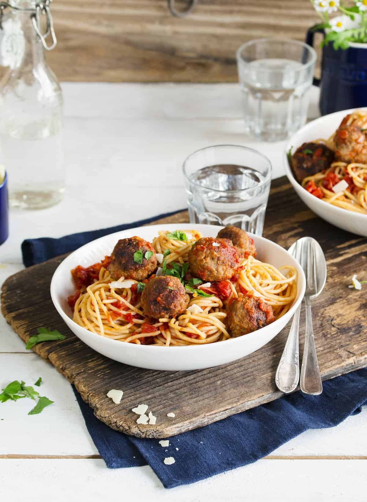 Zwei Teller mit Spaghetti und Hackbällchen in Tomatensoße auf einem Holzbrett angerichtet