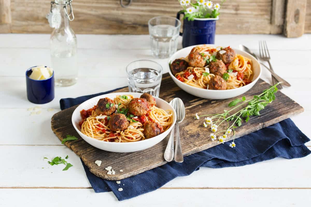 Zwei Teller mit Spaghetti und Hackbällchen in Tomatensoße auf einem Holzbrett angerichtet