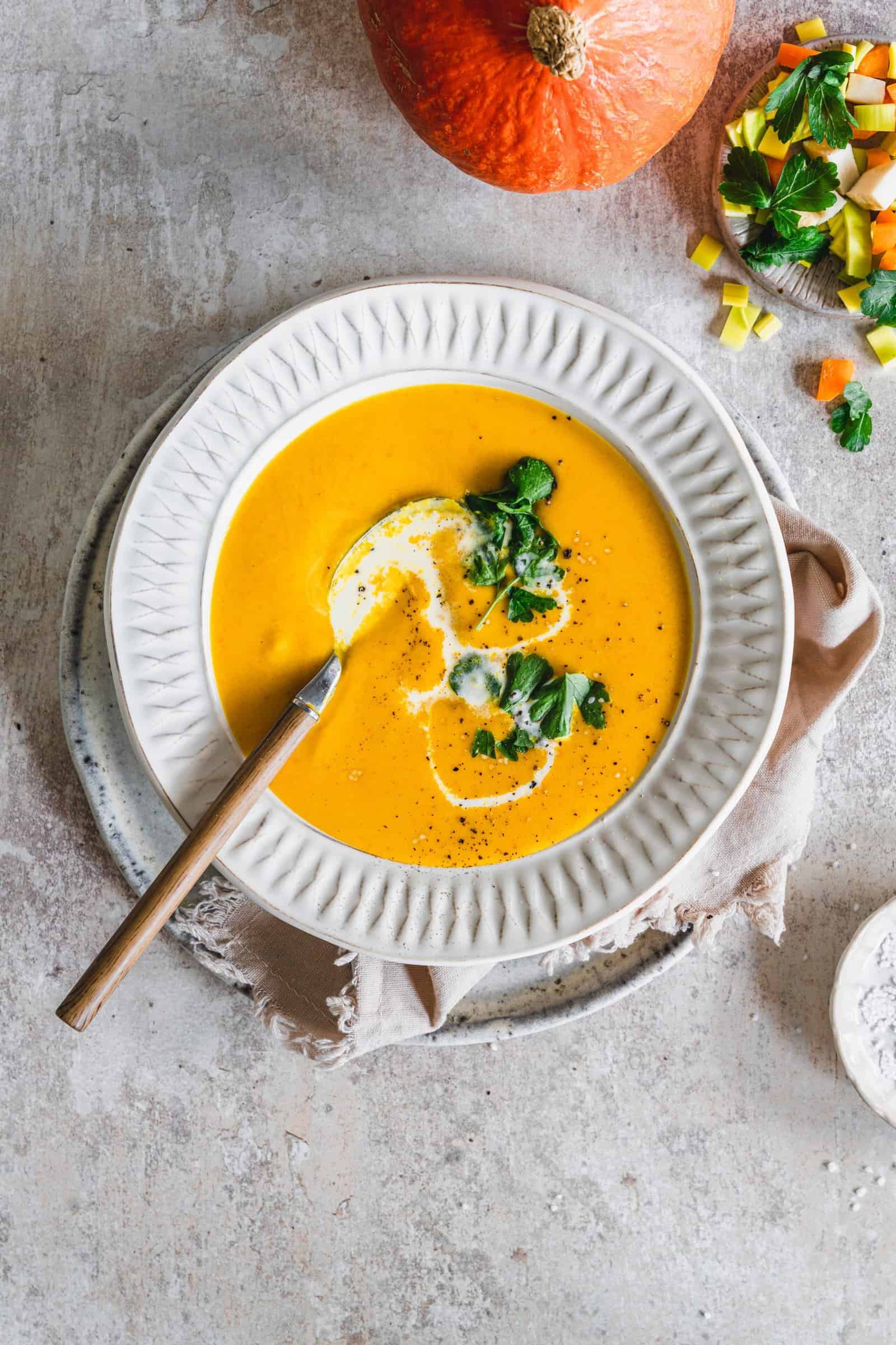 Kürbiscremesuppe von oben fotografiert auf einem hellen Teller, mit Sahne und Petersilie garniert – Foto: Tina Bumann