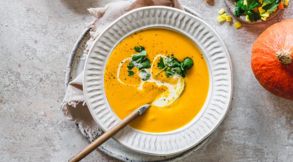 Kürbiscremesuppe von oben fotografiert auf einem hellen Teller, mit Sahne und Petersilie garniert – Foto: Tina Bumann