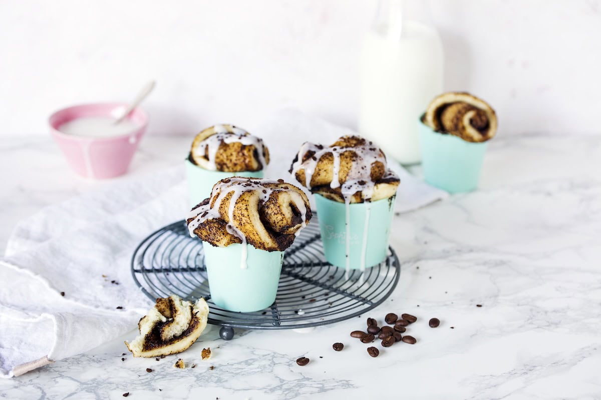 Mehrere Hefeschnecken in blauen Förmchen auf einem Gitter, daneben Kaffeebohnen