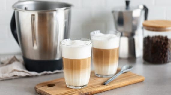 Zwei Gläser mit Kaffee und Milchschaeum, im Hintergrund der Mixtopf des Thermomix®