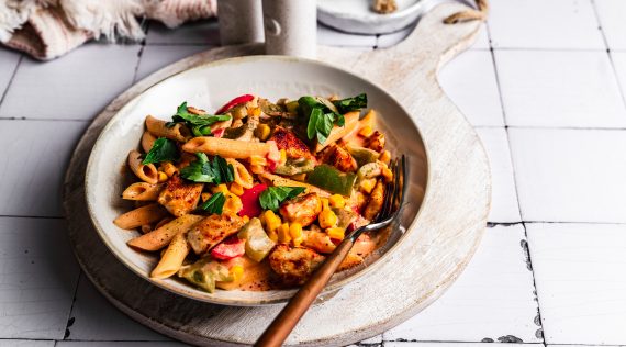 Teller mit Hähnchen-Nudelpfanne, mit Basilikum garniert, von oben fotografiert.